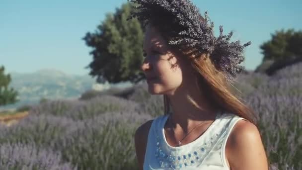 Mujer joven en corona de lavanda de pie en el campo de lavanda — Vídeos de Stock