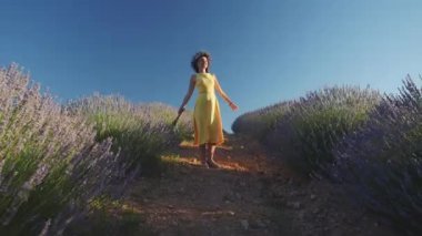 Lavanta tarlasında çelenk giymiş genç bir kadın dans ediyor.