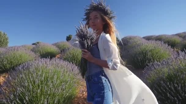 Young woman in wreath holding bouquet standing in lavender field — Stock Video