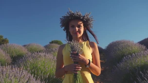 Jeune femme en couronne tenant bouquet debout dans le champ de lavande — Video