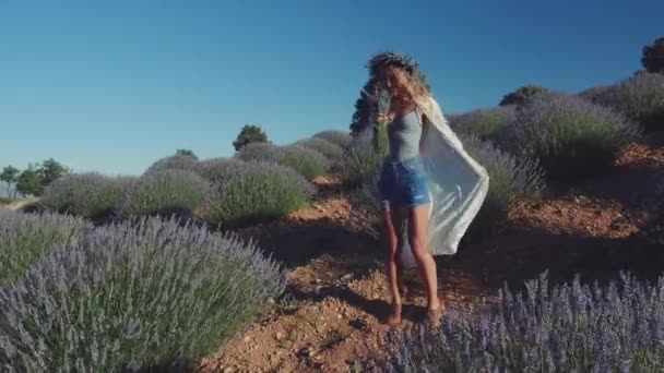 Молодая женщина в венке танцует на лавандовом поле — стоковое видео