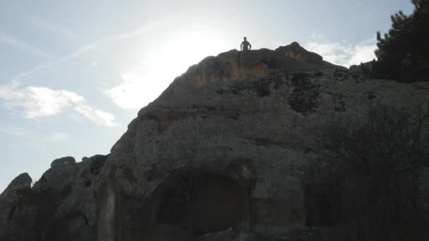 Мальчик стоит высоко на скале и смотрит вдаль — стоковое видео