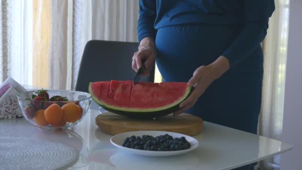 Молодая беременная женщина режет арбуз — стоковое видео