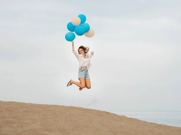Jeune femme sautant avec des ballons d'hélium bleu et blanc — Photo