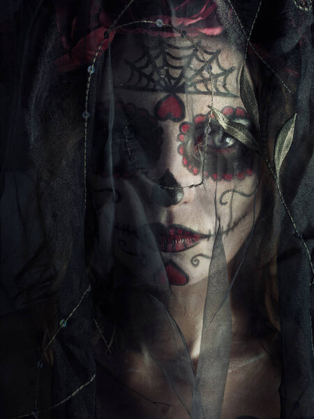 Studio portrait of Santa Muerte makeup woman standing behind the black transparent cloth on Halloween eve