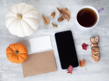 Boş beyaz kart, eski kağıt, akıllı telefon ve masanın üzerinde balkabaklarıyla sonbahar yaprakları. 