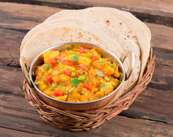 Indian Cuisine Spicy Fried Aloo Also Know as Potato Fry, Potato Curry, Aloo Masala or Alu Masala Served with Indian Bread, Roti or Chapati on Wooden Table
