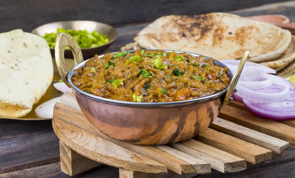 Indian Cuisine Sev Tamatar Also Called Sev Tamaeta or Sev Tameta is Served With Chapati, Papad, Onion or Raita. It is Made With Tomato And Onion Gravy With a Twist of Spicy Sev on Wooden Table