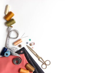 Dikiş aksesuarları ve kumaş üzerine beyaz bir arka plan. Dikiş ipliği, iğneleri, iğne, kumaş, düğmeler ve dikiş santimetre. Üstten Görünüm, flatlay 