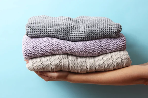 sweaters stacked in a pile in female hands on a colored background. Minimalism