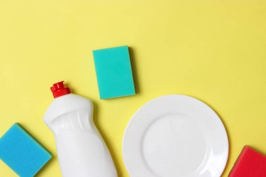 Bulaşık yıkama yardımcıları, Süngerler ve renkli bir arka planda bir plaka, üst görünüm. Ev işi, yemekleri yıka. flatlay