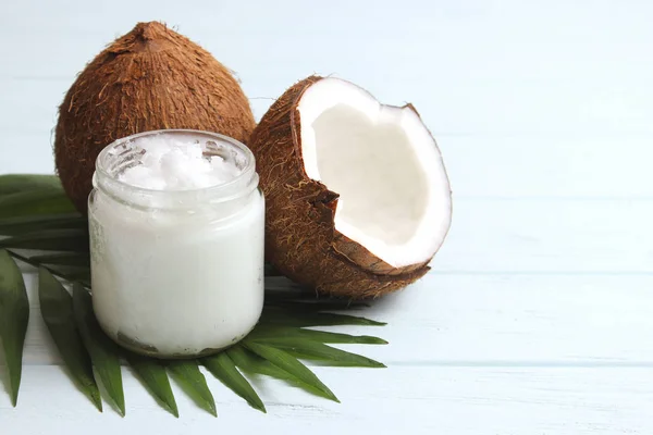 coconuts and coconut oil with tropical leaves on a wooden background