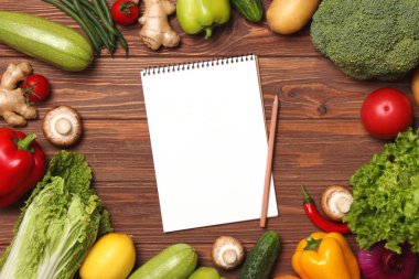 Farklı taze sebzeler ve tahta bir masanın üzerinde kağıt not defteri. Üst Manzara. Bir tarif, alışveriş listesi, satın alma ürünleri yaz. Yemek pişirmek. Düz Yatay 