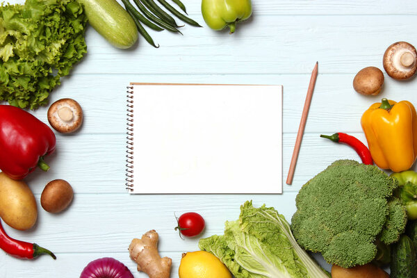 Different fresh vegetables and paper notepad on a wooden table. Top view. Write a recipe, shopping list, purchase products. Cooking. Flatlay 