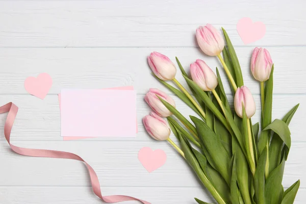 A bouquet of beautiful tulips and a card for text on a wooden background fork on top. Mother's day background, International Women's Day, birthday. Holiday, give.