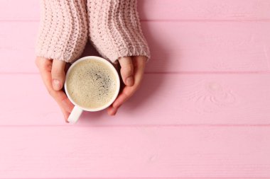 Bir fincan köpüklü kahve, kadın ellerinde, ahşap masada. Üst görünüm.