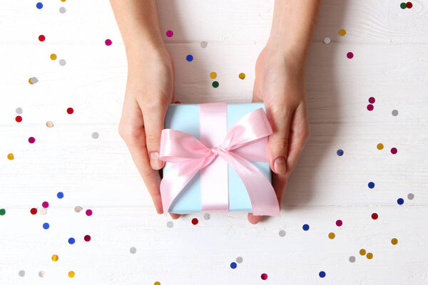 подарок в женских руках на цветном фоне с видом сверху на конфетти.