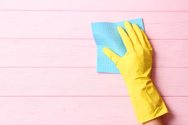 female hand in cleaning glove and rag on colored background