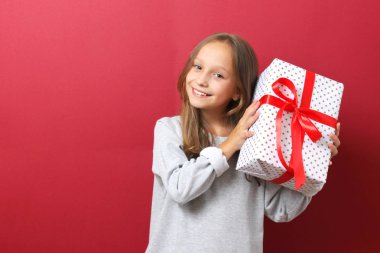 Renkli arka planda Noel şapkası takmış, elinde bir hediye tutan tatlı, neşeli bir kız.