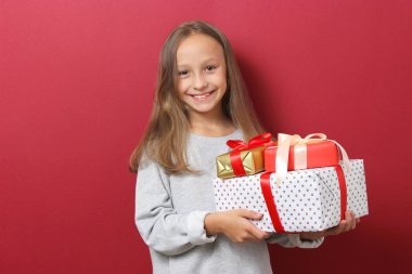 Renkli bir arka planda, Noel şapkası takmış, elinde hediyeler tutan sevimli, neşeli bir kız.