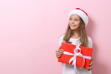 Renkli arka planda Noel şapkası takmış, elinde bir hediye tutan tatlı, neşeli bir kız.