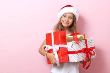 Renkli bir arka planda, Noel şapkası takmış, elinde hediyeler tutan sevimli, neşeli bir kız.