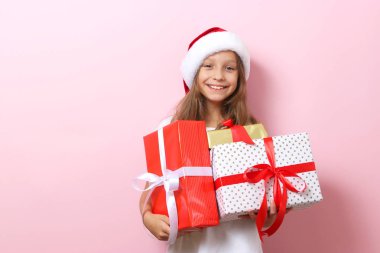 Renkli bir arka planda, Noel şapkası takmış, elinde hediyeler tutan sevimli, neşeli bir kız.