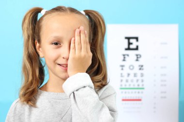 Küçük tatlı, neşeli kız göz doktorunun ofisinde göz testini geçiyor.