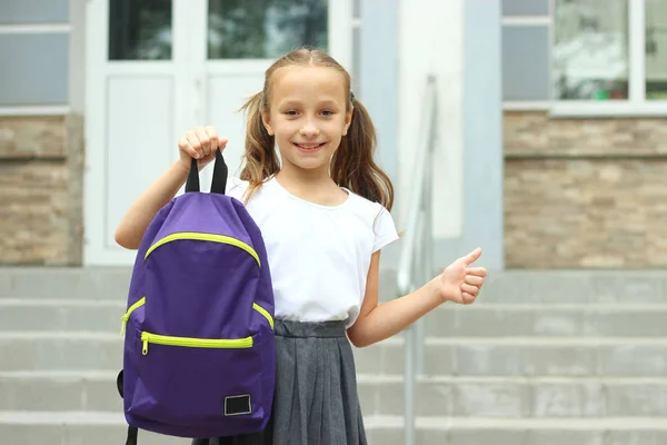 Cute schoolgirl with a school backpack in the schoolyard.