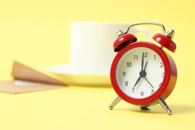 Renkli bir arka planda çalar saat, bir fincan kahve ve kırtasiye.