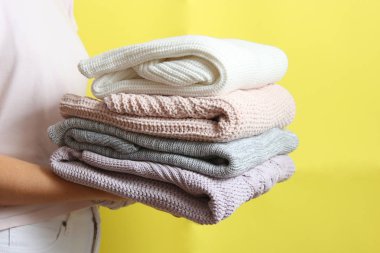 Renkli bir arka planda, kadınların elinde bir kazak yığını.