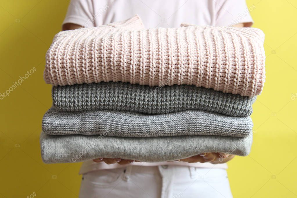 a stack of sweaters in women's hands on a colored background