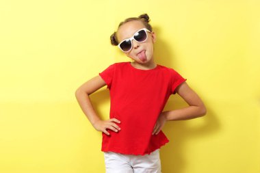 Renkli bir arka planda şık giyinmiş, güler yüzlü küçük bir kız. Çocuk kıyafetleri, çocuk modası.