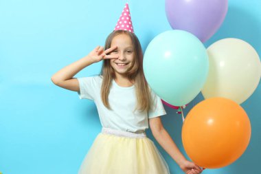Renkli arka planda balonları olan neşeli şapkalı şirin bir kızın portresi. Doğum günü, tatil.