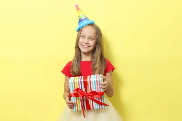 お祝いのキャップに小さな女の子の肖像画と色の背景に彼女の手の中に贈り物 誕生日 プレゼント — ストック写真