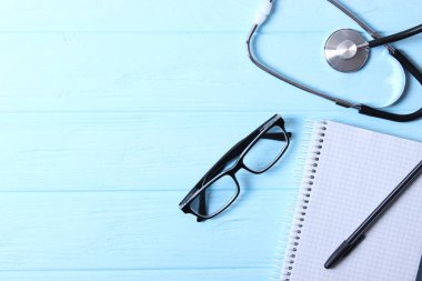 Doktorun masa üstü görüntüsü. Renkli arka planda farklı doktor aksesuarları. Haplar, gözlükler, steteskop ve defter..