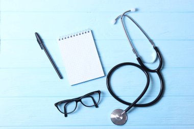 Doktorun masa üstü görüntüsü. Renkli arka planda farklı doktor aksesuarları. Haplar, gözlükler, steteskop ve defter..