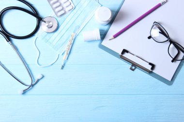 Doktorun masa üstü görüntüsü. Renkli arka planda farklı doktor aksesuarları. Haplar, gözlükler, steteskop ve defter..