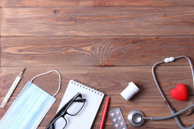 Doktorun masa üstü görüntüsü. Renkli arka planda farklı doktor aksesuarları. Haplar, gözlükler, steteskop ve defter..