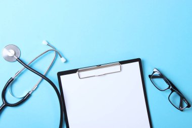 Doktorun masa üstü görüntüsü. Renkli arka planda farklı doktor aksesuarları. Haplar, gözlükler, steteskop ve defter..