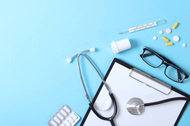 Doktorun masa üstü görüntüsü. Renkli arka planda farklı doktor aksesuarları. Haplar, gözlükler, steteskop ve defter..