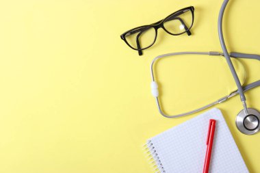 Doktorun masa üstü görüntüsü. Renkli arka planda farklı doktor aksesuarları. Haplar, gözlükler, steteskop ve defter..