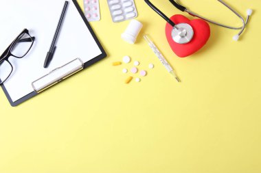 Doktorun masa üstü görüntüsü. Renkli arka planda farklı doktor aksesuarları. Haplar, gözlükler, steteskop ve defter..