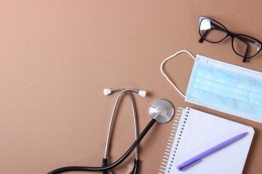 Doktorun masa üstü görüntüsü. Renkli arka planda farklı doktor aksesuarları. Haplar, gözlükler, steteskop ve defter..