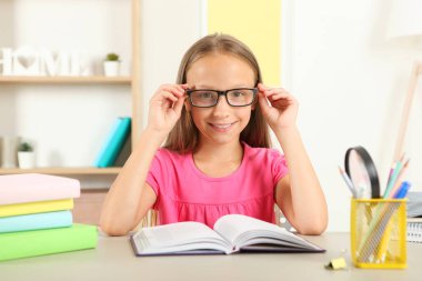 Gözlüklü küçük kız evde kitap okuyor.