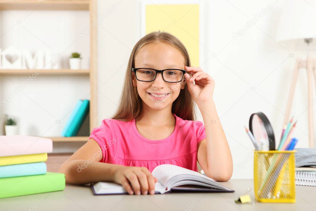 Little girl with glasses reading a book at home