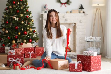 Genç ve güzel bir kız dekore edilmiş ev içinde noel hediyelerini paketliyor.