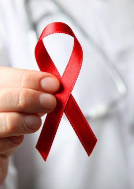  Kırmızı kurdele, beyaz önlüklü bir doktorun elindeki AIDS ve prezervatifleri simgeliyor. Dikey fotoğraf biçimi