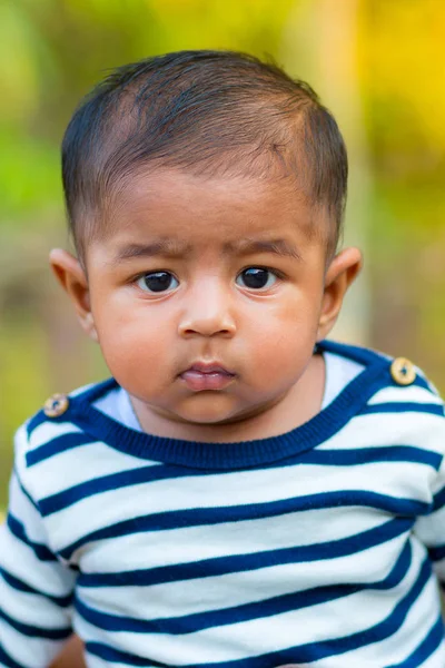 Bir bebek erkek bebek bakıyor ve gülümsüyor. Giyinmiş beyaz ve lacivert çizgili elbise vardır. Bebek samimi ateş. Bebek portresi.