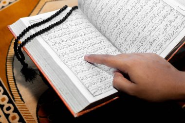 Müslüman kadın Kuran 'ı parmağıyla okuyor. Duaların üzerine Kur 'an-ı Kerim. Yakın çekim görüntüleri. İçeride. Ellere odaklan..
